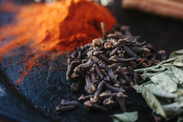 Black cloves spice over black plate surrounded by spices.