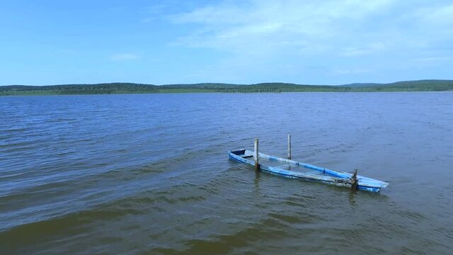 A wooden old boat of blue color on the waves of the lake is filled with water.
