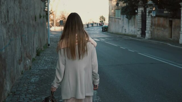 Back view of young lady walking in the city centre alone. Female with long hair going near the road, enjoying the day.
