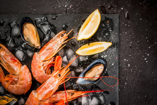 Prepared for cooking dinner seafood - shrimp and mussels on ice, on a cutting slate board, with lemon and seasonings. Top view, copy space