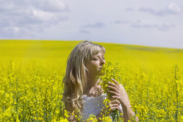 Naklejka na ściany i meble Beautiful dreamy woman in a rapeseed field with a bouquet dreams and enjoys nature.