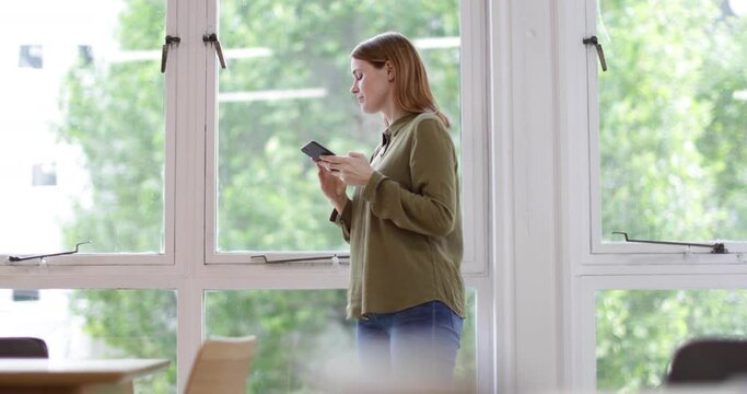 Businesswoman in office looking out of the window and at smartphone