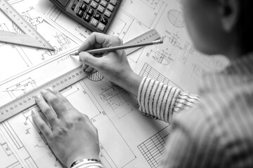 Girl architect draws a plan, graph, design, geometric shapes by pencil on large sheet of paper at...