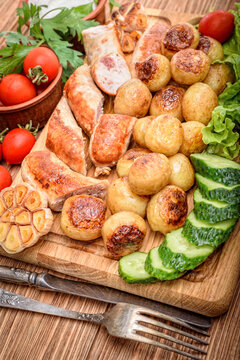 Grilled sausages and vegetables on the wooden board.