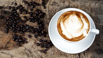 Hot cappuccino or latte art. A cup of coffee with milk put on a wood table with dark roasting coffee beans and cinnamon. Latte art by milk. Decorated with flowers.