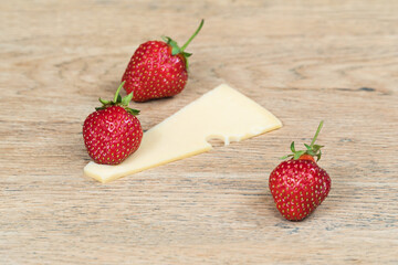 Ripe strawberry and piece of holey cheese on old wooden table