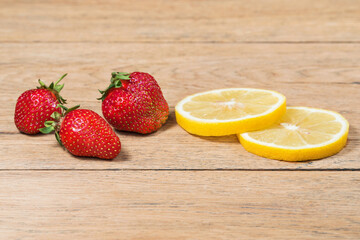 Berries of ripe strawberries and two slices of lemon on an old wooden table