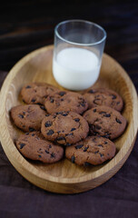 Chocolate chip cookies on dark background with glass of milk
