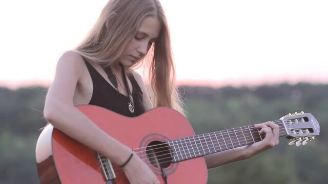 Beautiful girl playing acoustic guitar at sunset outdoors