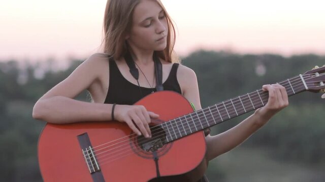 Girl playing acoustic guitar at sunset, tilt down
