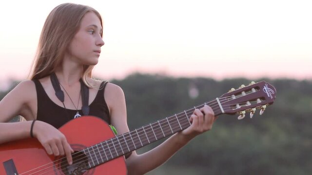 Young pretty woman relaxing with the guitar at sunset outdoors, panning camera