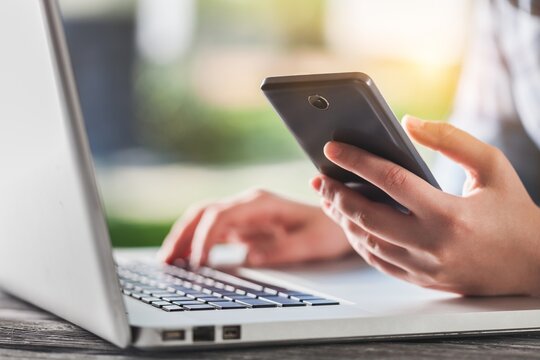 Human with phone works on laptop.