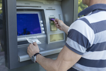 Naklejka na ściany i meble Man taking money from a cash machine using credit card. Cash widrow and finance concept