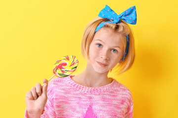 Funny teenager girl holding colourful lollipop on yellow background