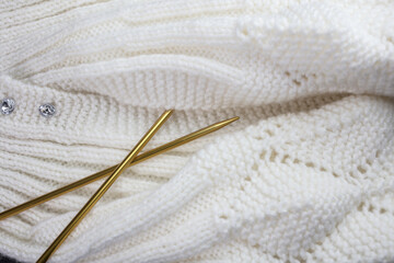 White knitted garment with gold colored knitting needles
