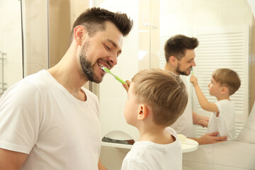 Cute little boy helping his father to brush teeth near mirror in bathroom