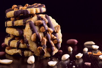 Cookies with peanuts, covered with chocolate icing, on a dark wooden background with space for text.