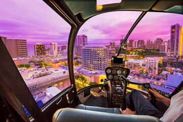 Fototapeta na wymiar Pink light at twilight of Waikiki cityscape in Oahu island, Hawaii, United States. City night lights and nightlife concept. Helicopter cockpit with pilot arm and control console inside the cabin.