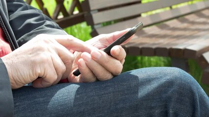 Elderly Man Sitting On Park Bench And Messaging On Mobile Phone
