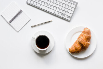 Business breakfast in office with notebook, coffee and croissant on white table background top view mock-up