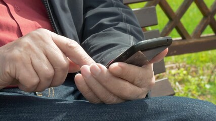 Elderly Man Sitting On Park Bench And Messaging On Mobile Phone