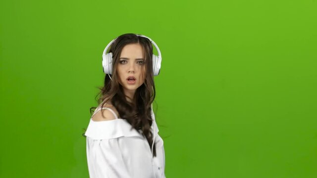 Girl listens through the headphones music and whirl around her. Green screen