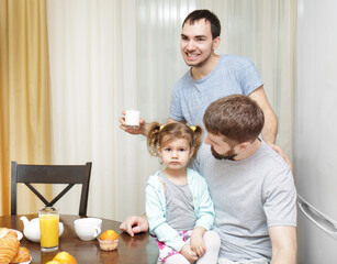 Male gay couple with daughter having breakfast in kitchen