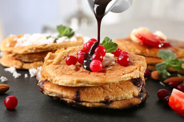 Pouring sweet sauce from gravy boat onto stack of delicious coconut pancakes with berries