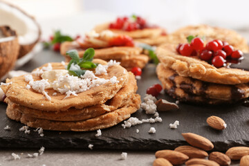 Stacks of delicious coconut pancakes with sweet sauce, berries, shavings and mint on slate plate, close up