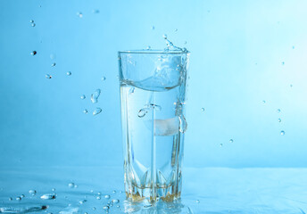 Ice dropped in a glass of water, falling in, making a splash and water droplets