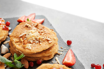 Stack of delicious coconut pancakes with berries and shavings on slate plate, close up