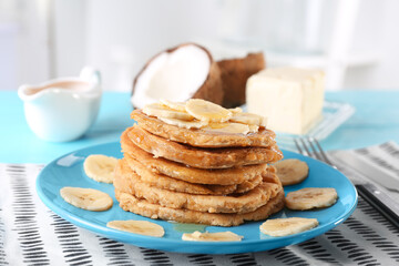 Stack of delicious coconut pancakes with sweet sauce and sliced banana on table