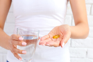 Woman holding fish oil pill and glass of water, closeup
