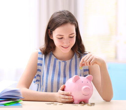 Young girl putting coin into piggy bank on light background. Saving for education concept