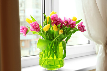 Glass vase with bouquet of beautiful tulips on windowsill