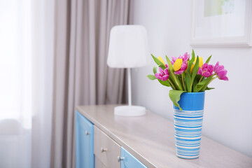 Vase with bouquet of beautiful tulips on chest of drawers