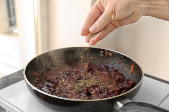 Female hand sprinkling herbs on beans in frying pan