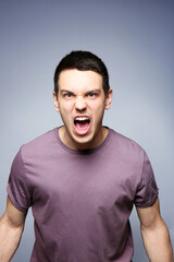 Handsome angry young man on gray background