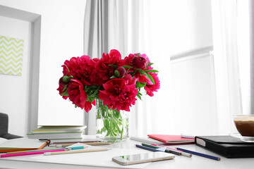 Vase with beautiful peonies, stationery and mobile phone on light table