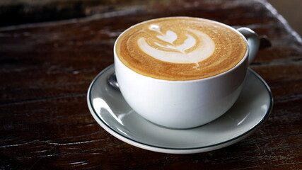 Hot cappuccino or latte art coffee. A cup of coffee on the wooden table. Morning breakfast with coffee. Latte art created by pouring steamed milk.