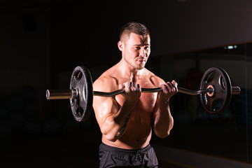 Fototapeta na wymiar Sporty man doing exercises with barbell on dark background
