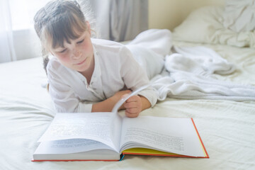 indoor portrait of young european girl lying in bed and reading a book