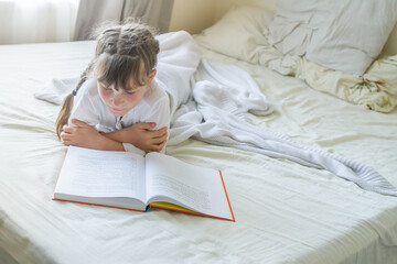 indoor portrait of young european girl lying in bed and reading a book