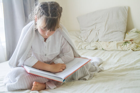 indoor portrait of young european girl lying in bed and reading a book