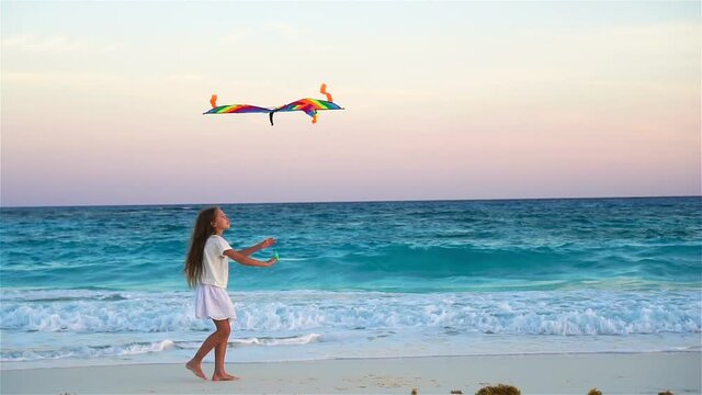 Little girl with flying kite on tropical beach. Kid play on ocean shore. Child with beach toys in slow motion