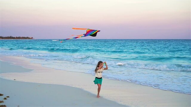 Little girl with flying kite on tropical beach. Kid play on ocean shore. Child with beach toys in slow motion