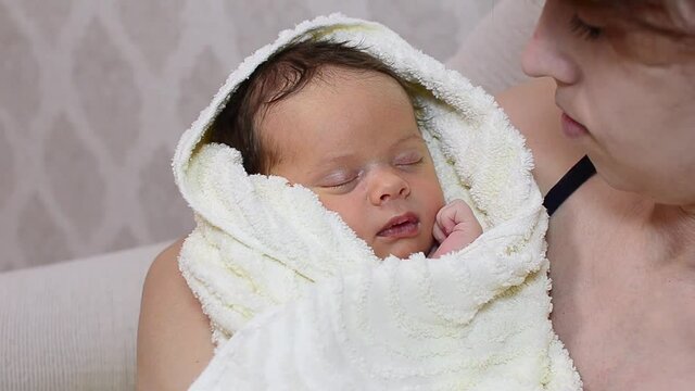 baby sleeps in her mothers arms wrapped in white towel, mother kissing baby