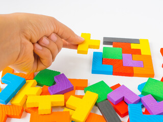 hand holding the last piece to complete a square tangram puzzle colorful wooden puzzle for kid on...