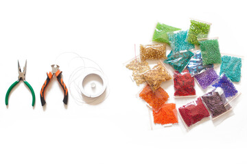 Colorful beads, pliers and bijouterie lie on a white background.