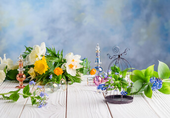 flowers and perfume bottles on a white wooden table with decorative cage on a blue pastel background